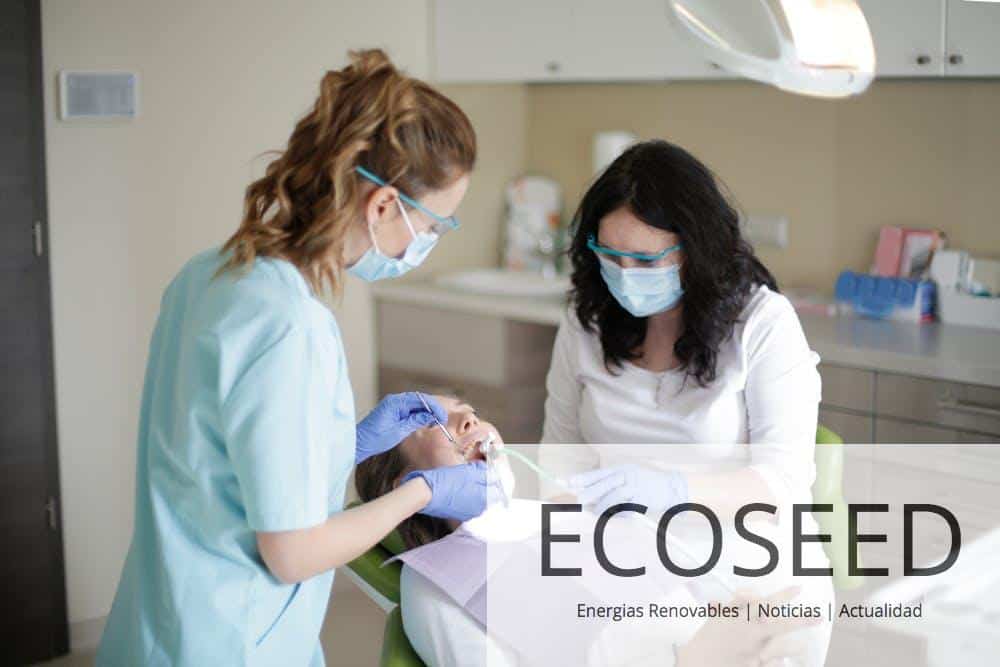 Side view of female dentist in mask wearing blue uniform with latex gloves and protective glasses and assistant using dental tools for examining teeth of female patient lying in dental chair