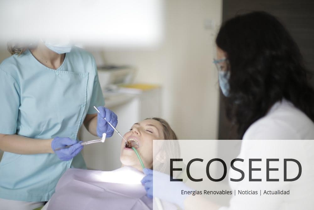 Crop faceless female dentist in blue uniform and latex gloves inserting cotton tampon to patient mouth while working with assistant and preparing patient for dental treatment